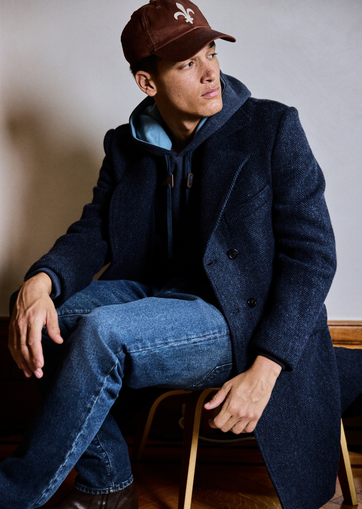 Model wears the Bowery Coat layered over a hoodie and a cap.