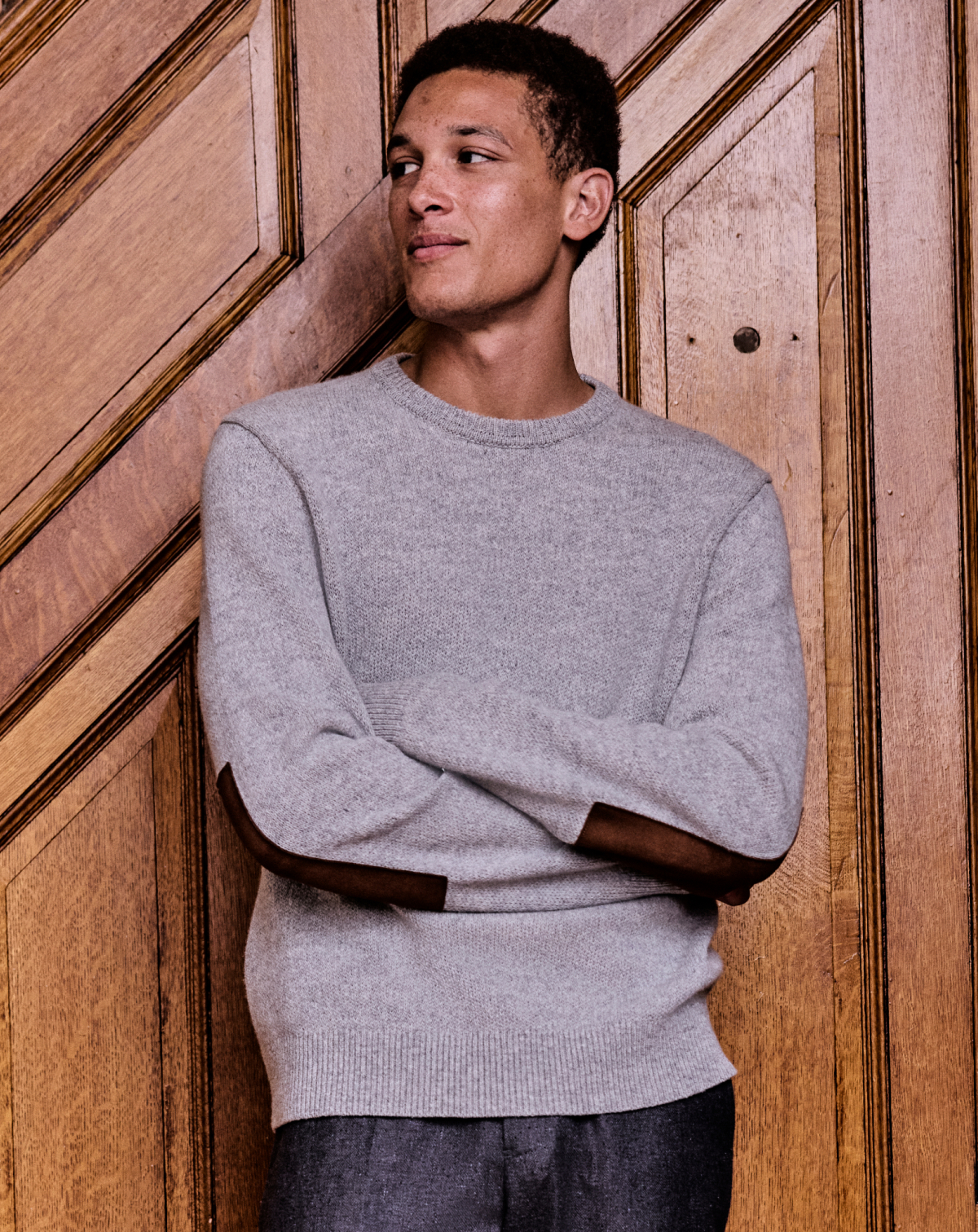 Model wears the Luxury Dover Sweater against a wood panel backdrop.