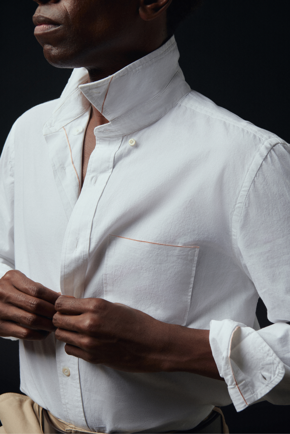 Man buttons a white shirt against a black background.