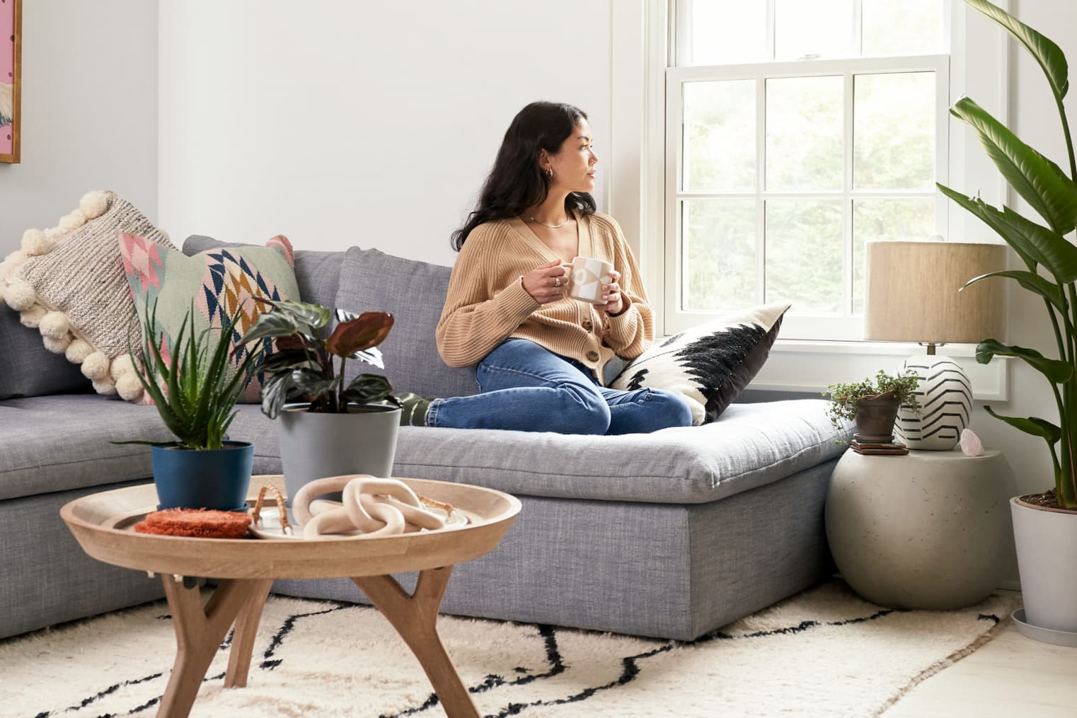 woman on sofa, drinking tea, surrounded by plants