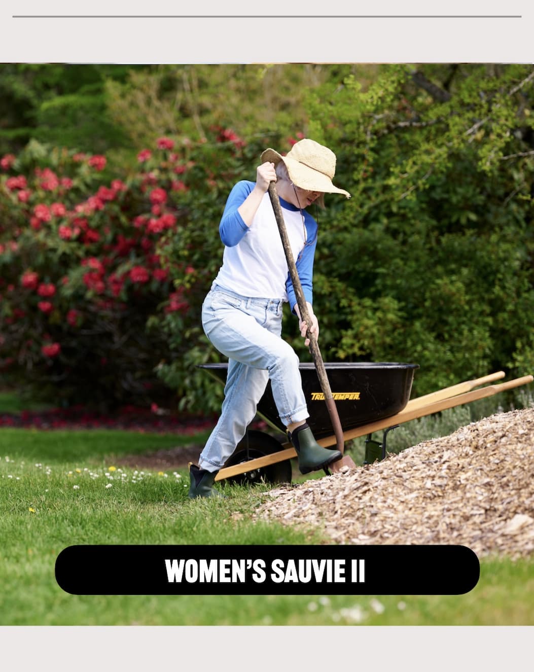 A woman shoveling mulch with a wheel barrow in the background. Shop our Sauvie II chelsea.