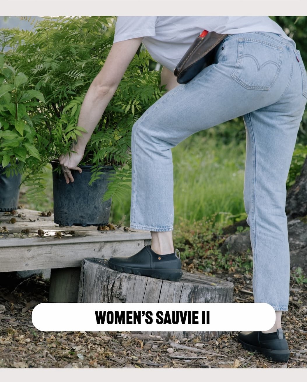 A woman picking up a tree bucket. Shop our Women's Holly Rain zip 