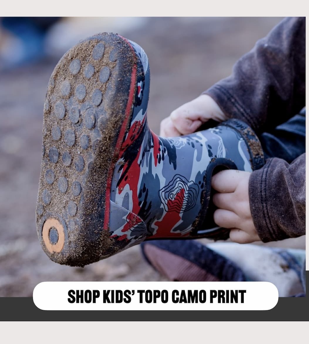 Closeup of a kid pulling on his Skipper Topo Camo print rainboots