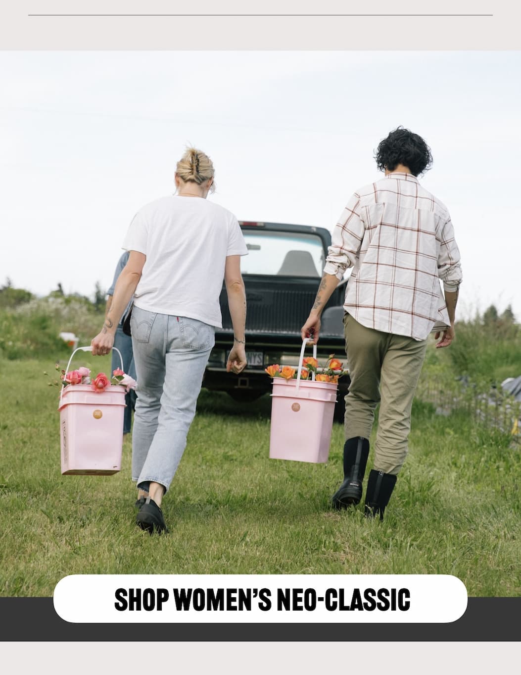 Two women carrying a pink bucket of flowers to a truck bed. Shop our Neo-Classic