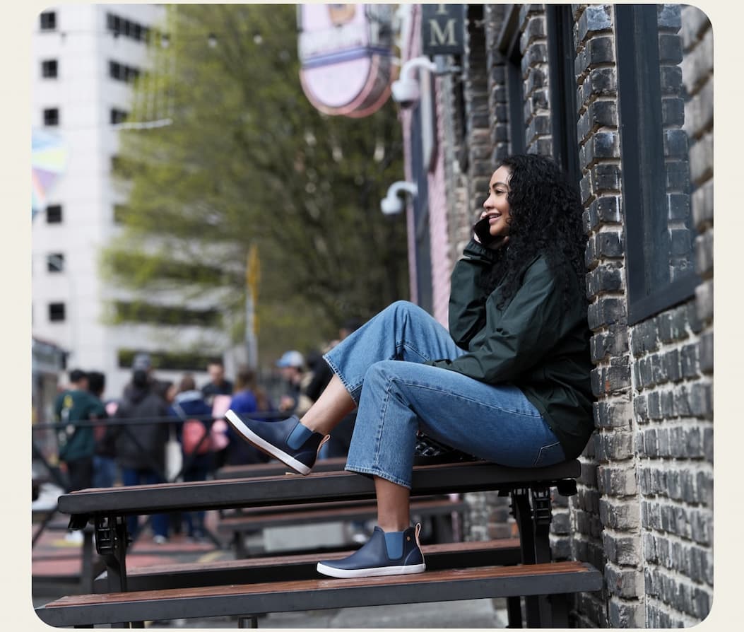 Image shown is a woman talking on a phone in the city. Shop our Women's casual waterproof shoes.