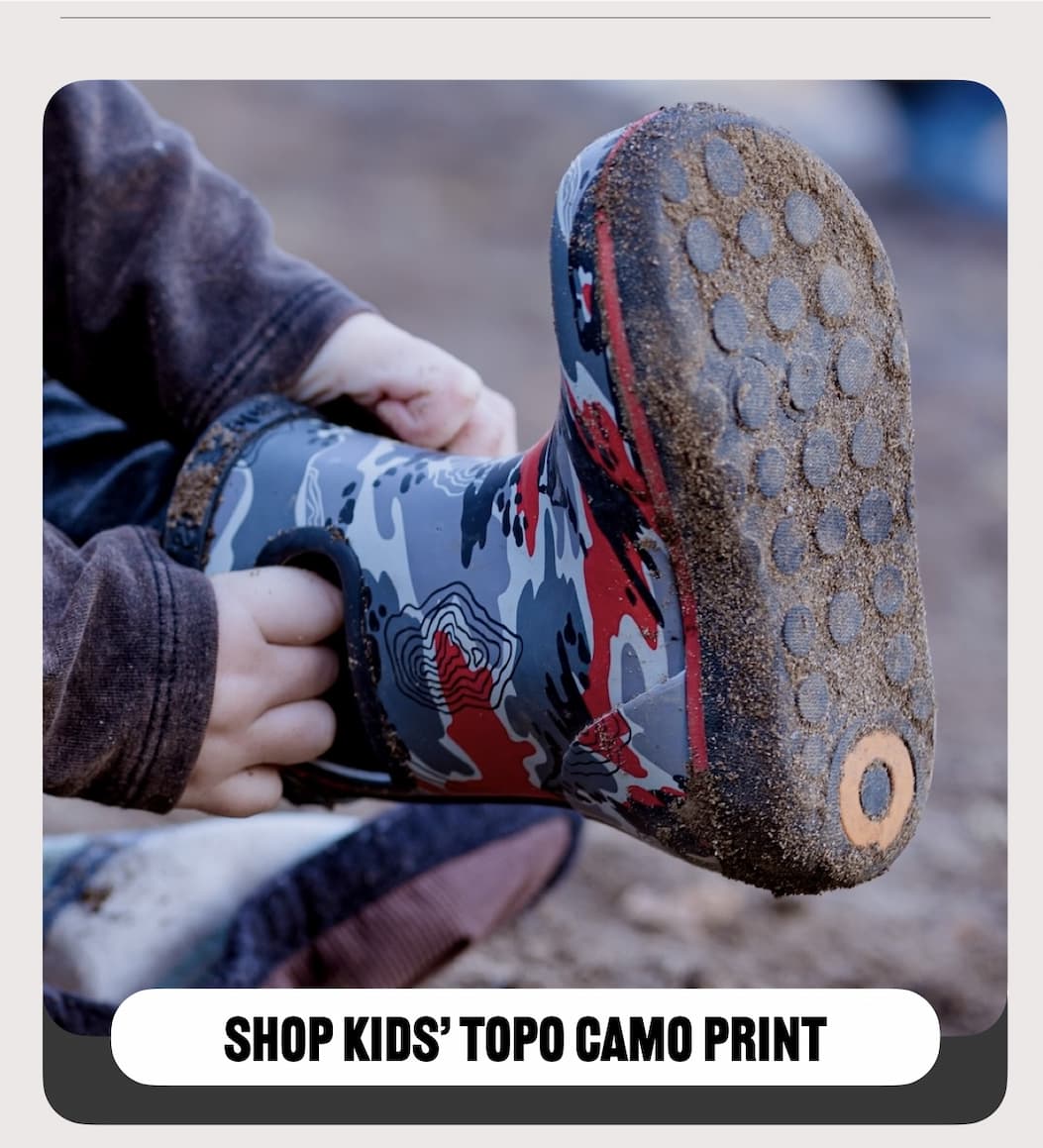 A kid putting on his topo camo print rainboot