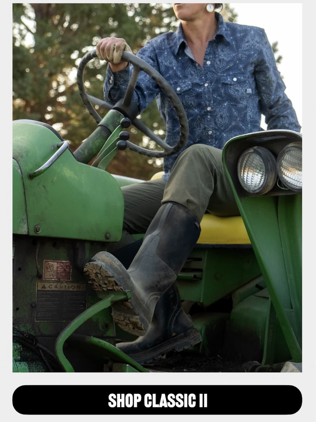 A woman driving a tractor wearing the Classic II boot.  Shop this style.