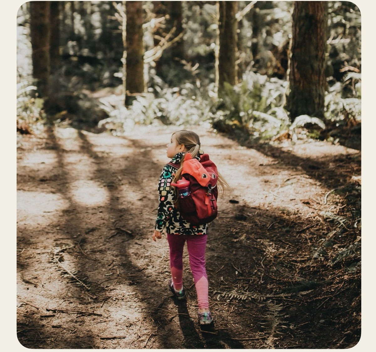 A girl walking through the forest wearing a backpack. 