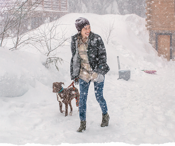 A woman walking in snow with her dog.