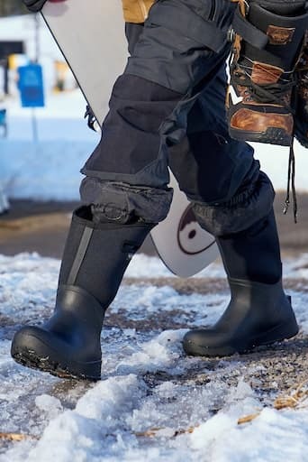 A man walking in his bozeman ii boots holding a snowboard.