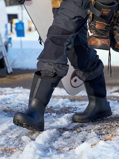 A man walking in his bozeman ii boots holding a snowboard.