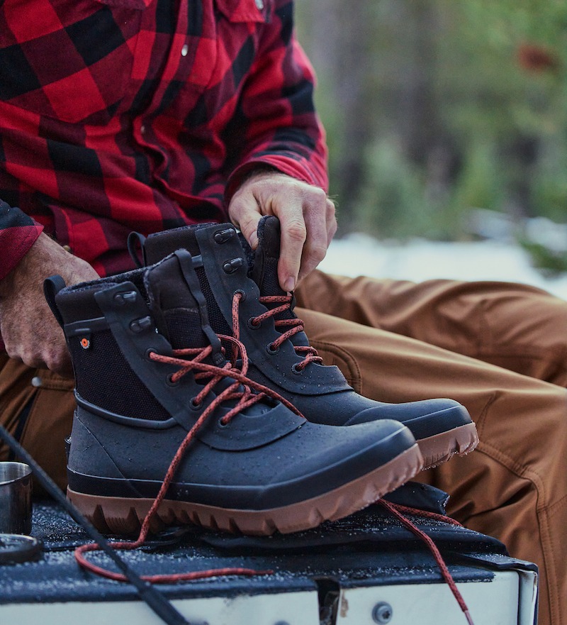 A man grabbing his Arcata Lace boots in brown with red laces