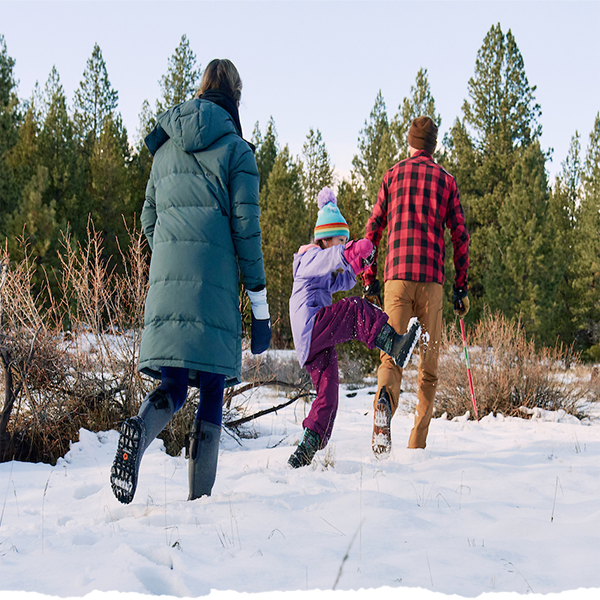A family walking through a winter field wearing bogs.