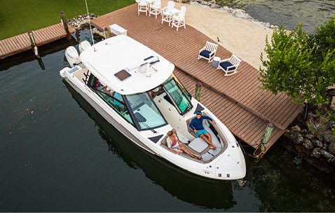 A couple relaxes on a white motorboat docked at a wooden pier.