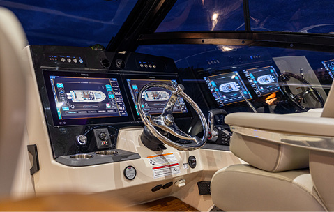 The helm of a boat, featuring two Simrad navigation screens, a steering wheel, and a captain's chair.