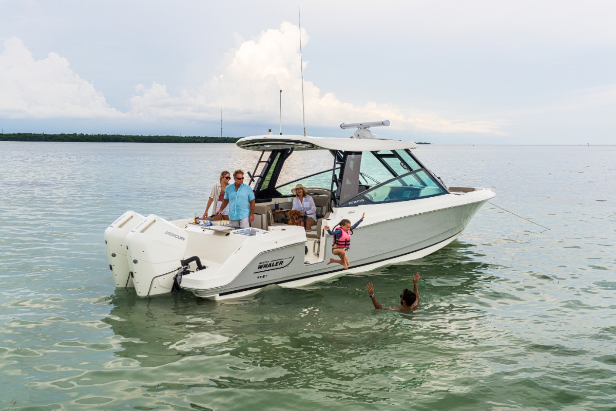 Family fun on a Boston Whaler boat.  A child jumps into the calm water to swim with a man as two adults and a dog watch from the deck.