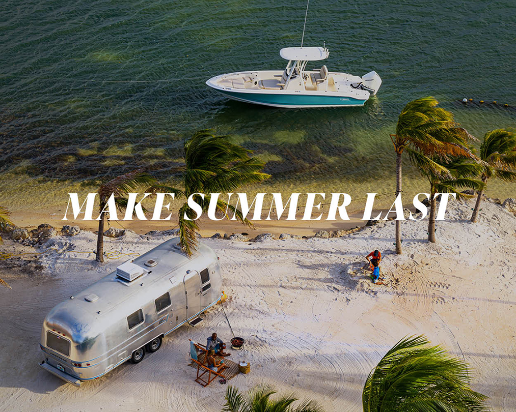 A picturesque tropical setting with a boat anchored in clear water, an RV parked on the sand, and people enjoying the outdoors, with the message "MAKE SUMMER LAST".
