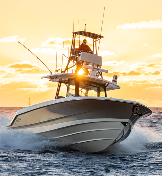 Modern Boston Whaler boat with a captain at the helm, cutting through waves during a golden hour sunset.