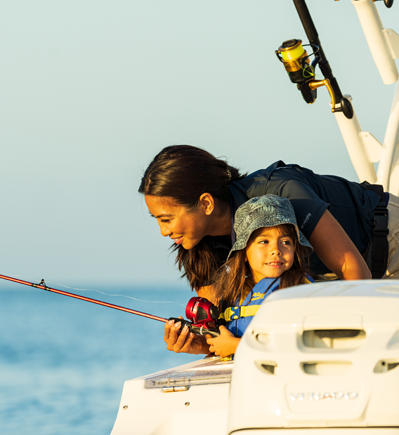 A woman and a young girl fishing from a boat, both looking intently at the fishing line.