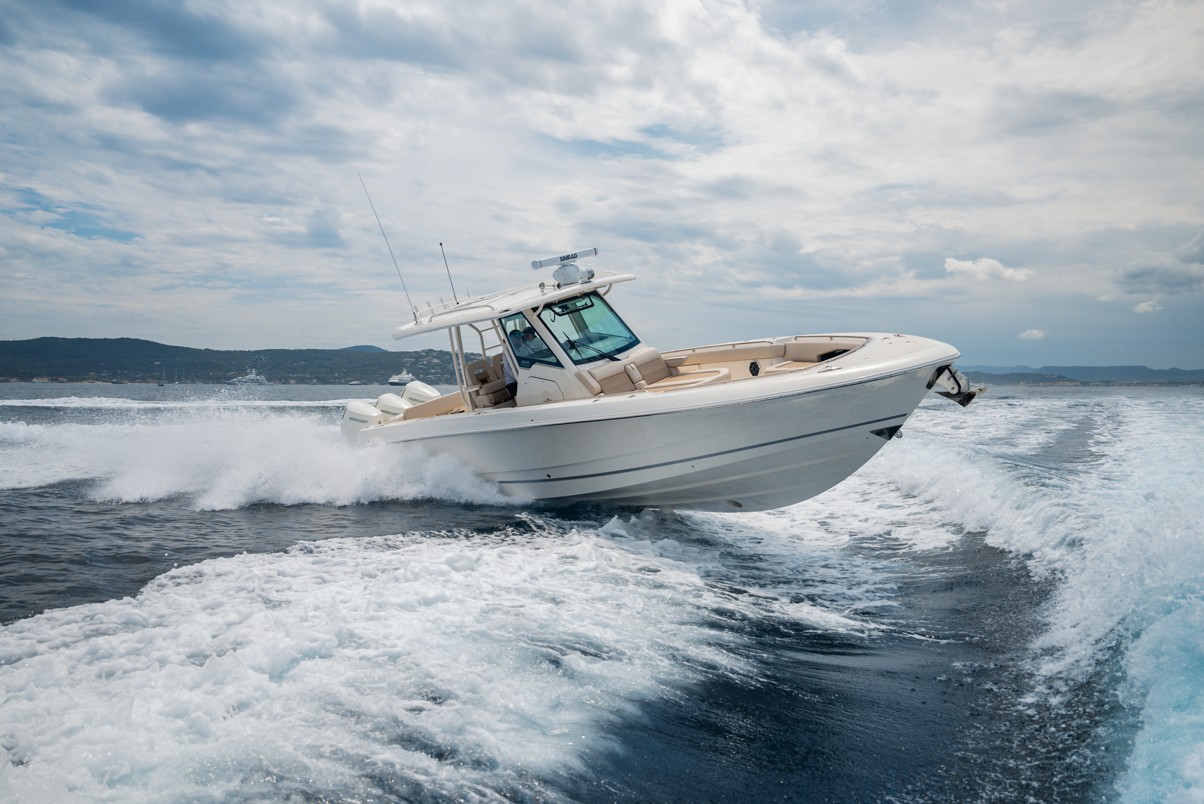 A sleek white Boston Whaler with multiple outboard engines skips across the ocean waves, kicking up a dramatic spray of water.