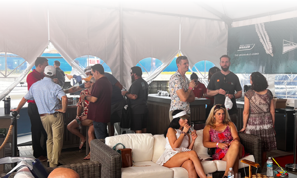 A group of people socializing under a white tent with a Boston Whaler banner in the background.