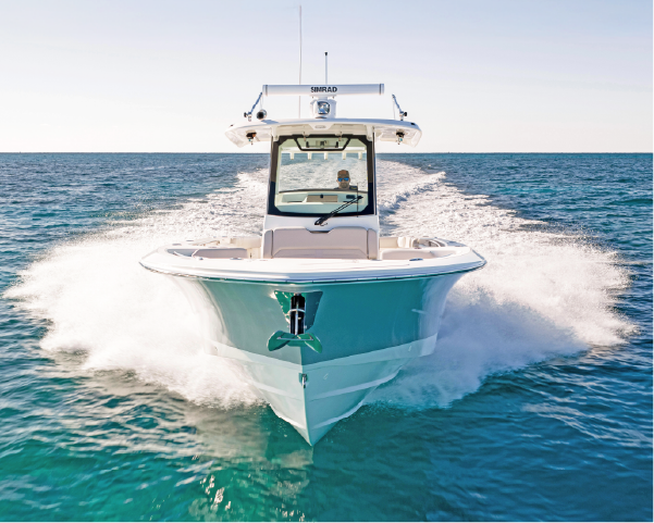 A white and teal boat speeds across clear blue water, creating a large wake on a sunny day.