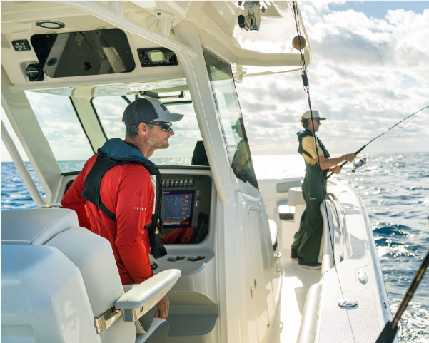 Two men fishing from a white boat on the open ocean under a partly cloudy sky.