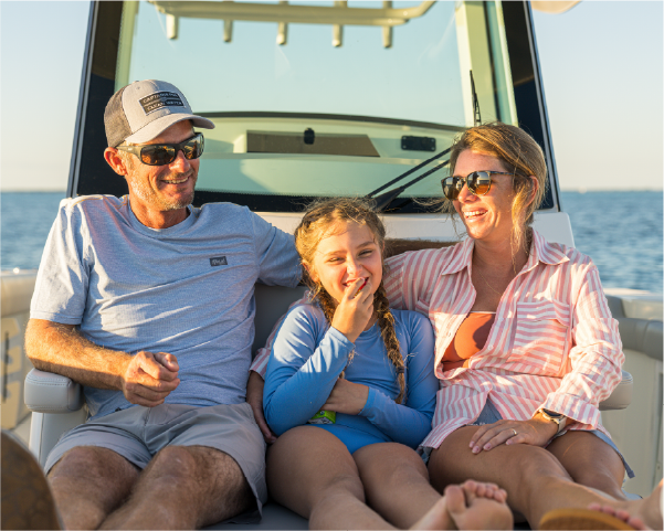 A happy family of three, a man, woman, and young girl, smiling and laughing together on a boat.