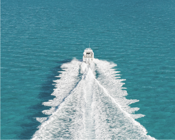 Aerial view of a boat cruising through clear blue-green ocean, creating a distinct white trail.