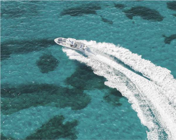 Aerial view of a white boat speeding across clear turquoise water, leaving a large white wake.
