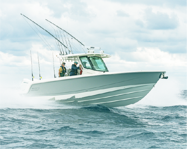 A white and grey fishing boat with two people on board speeds across choppy water, kicking up spray.