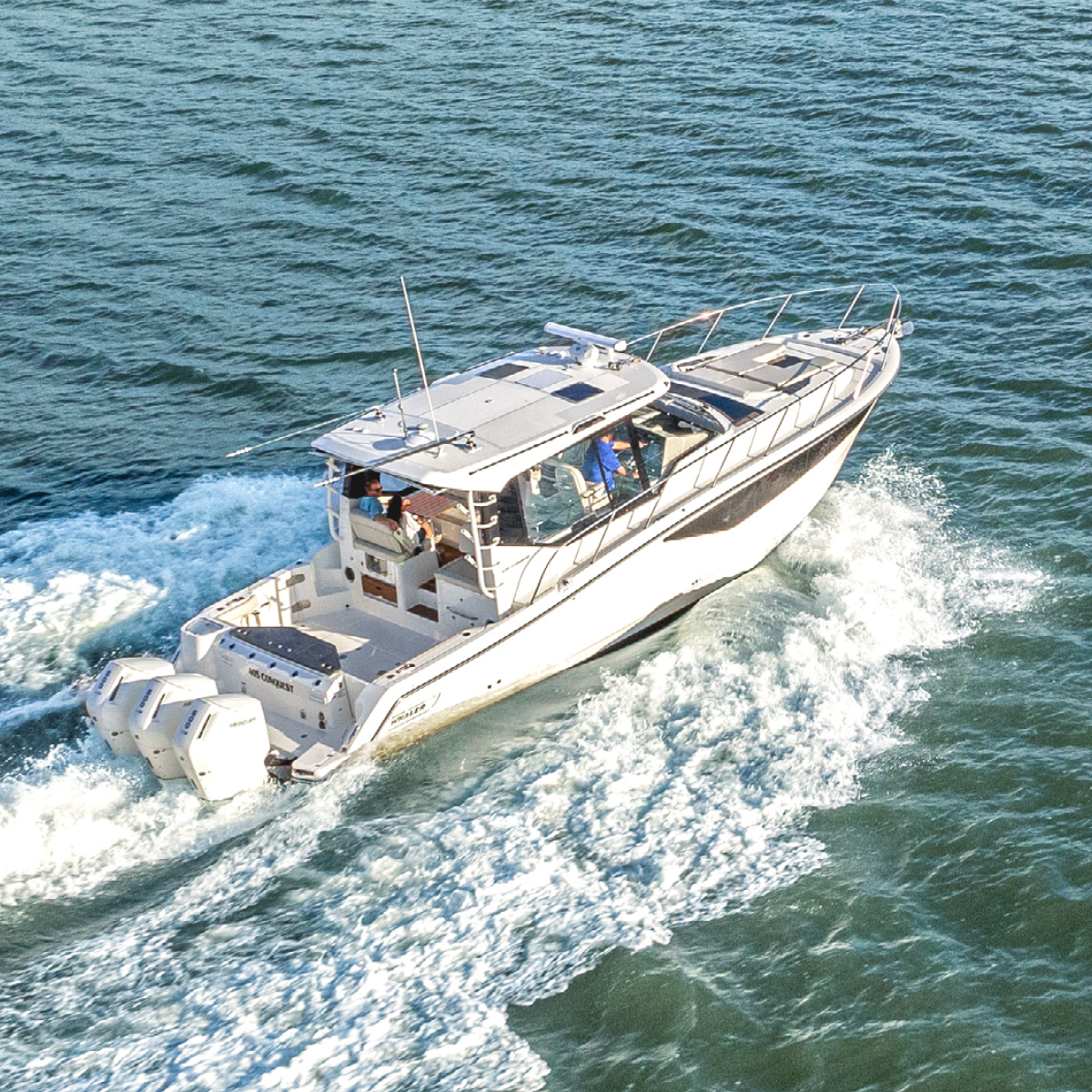 A white Boston Whaler 405 Conquest boat with four outboard motors speeds across blue water, creating a large wake.