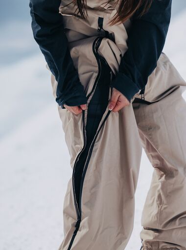 The Burton Futuretrust 2L Bib Pants in beige on a Burton Rider at a mountain on a sunny day