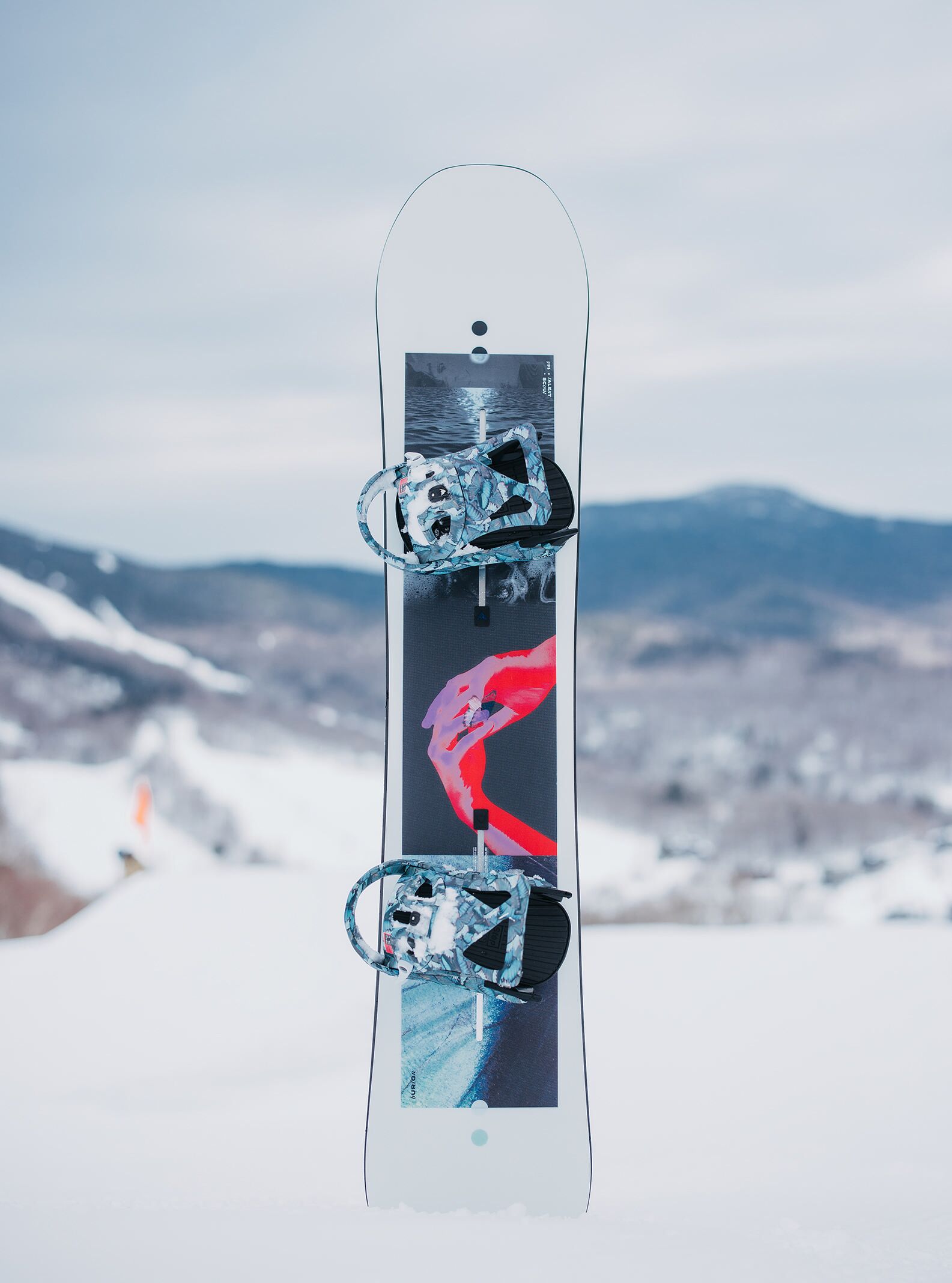 The Women's Burton Talent Scout Camber Snowboard in the snow with mountains in the background