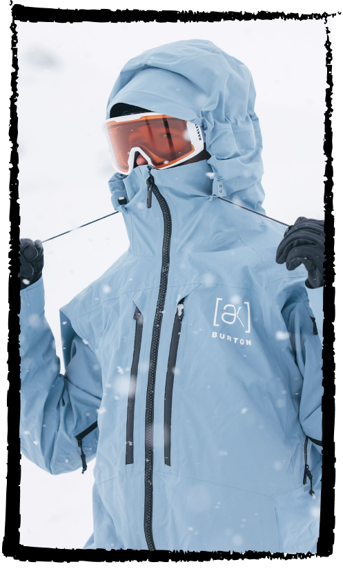Snowboarder wearing the Burton [ak]® Swash jacket in dusty blue in the mountains