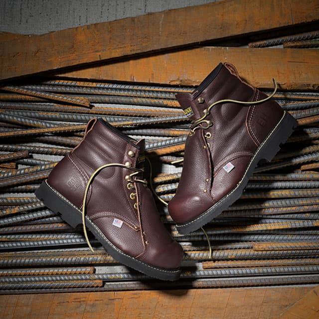 The Int Lo 6" Met Guard Steel Toe Heavy Duty Work Boots in brown laying on metal rods and wood. Shop men's met guard.