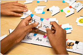 Students hands holding sentence puzzle pieces at a classroom table.