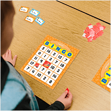 Young boy sitting at a table in a classroom playing Addition & Subtraction Bingo.