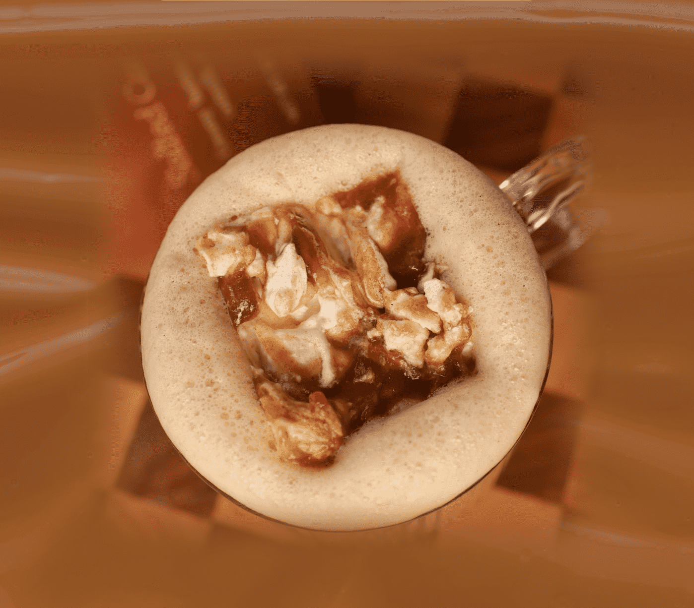 Top-down close-up view of a frothy chai latte mug topped with a large, homemade swirled date caramel marshmallow.