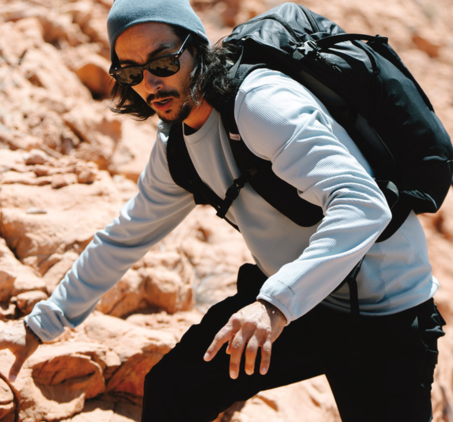 A man scrambling through rocks in a sun hoodie.
