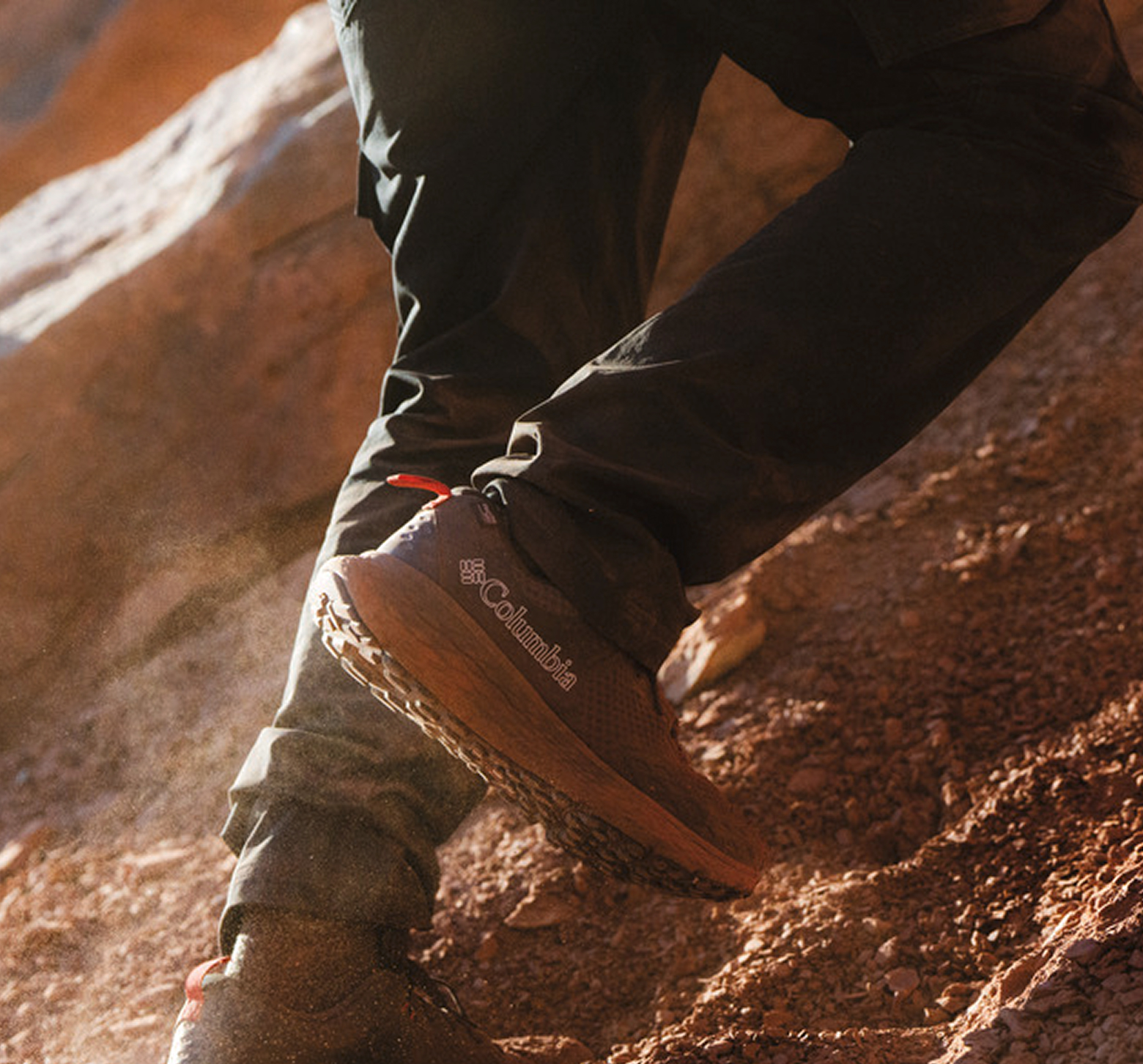 A knee down image of a trail shoe on rocky terrain.