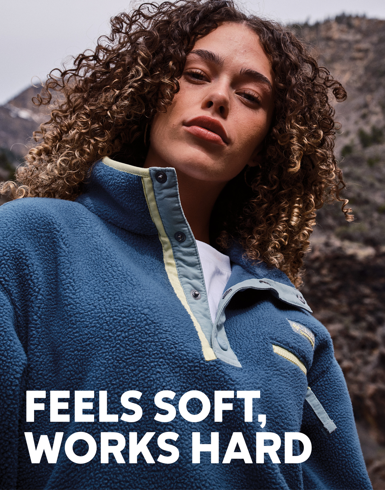 A woman wearing a blue fleece pullover with text: FEELS SOFT, WORKS HARD