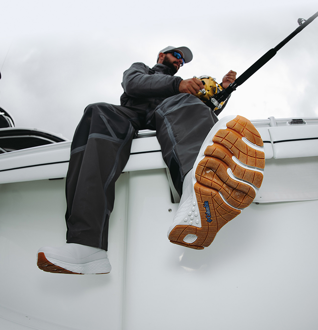 An angler sitting on the side of a boat, wearing white PFG sport boots.