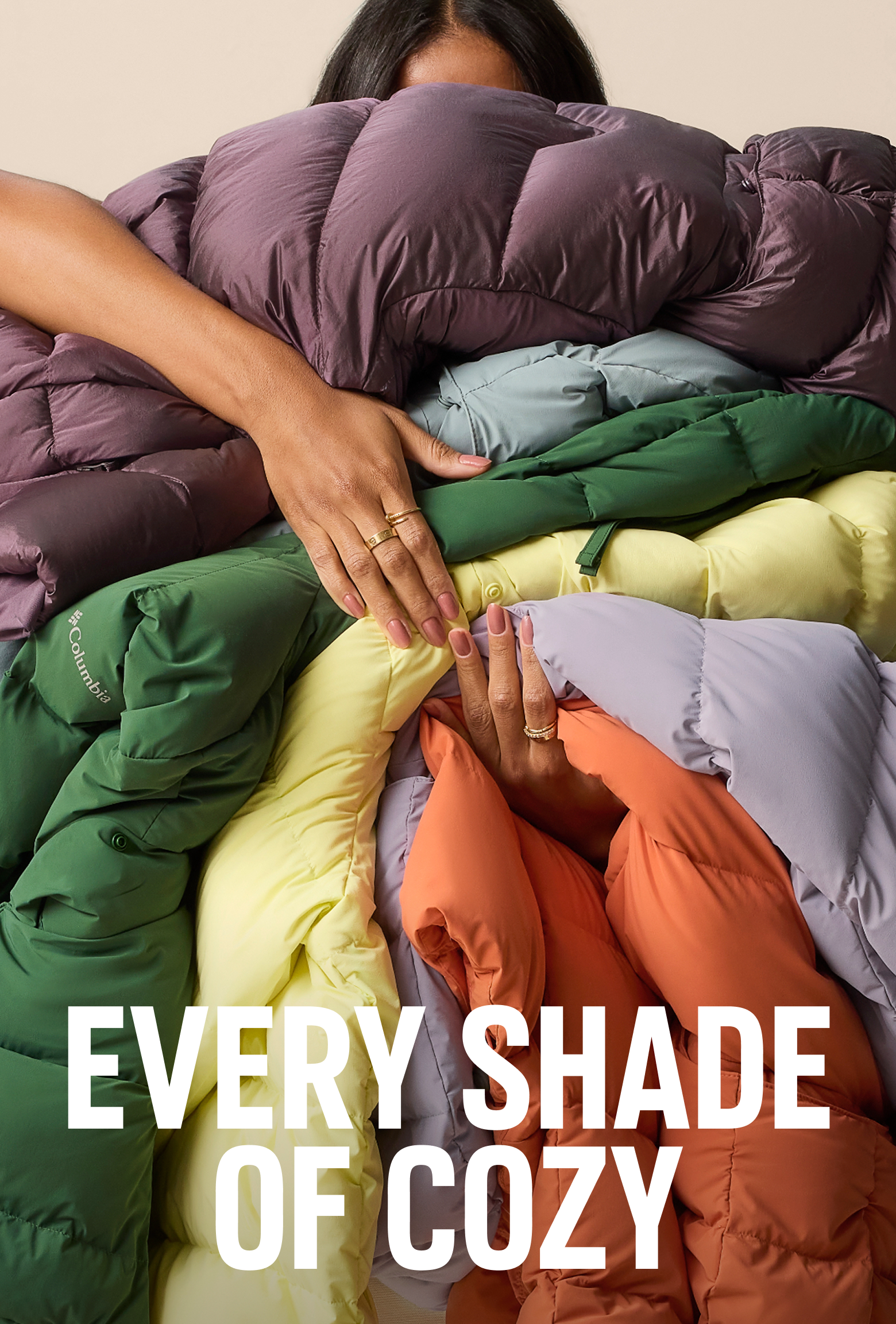 A woman holding many colorful jackets with text: EVERY SHADE OF COZY