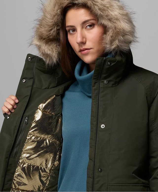 A woman wearing a dark green parka, opening up her jacket to reveal the gold interior.
