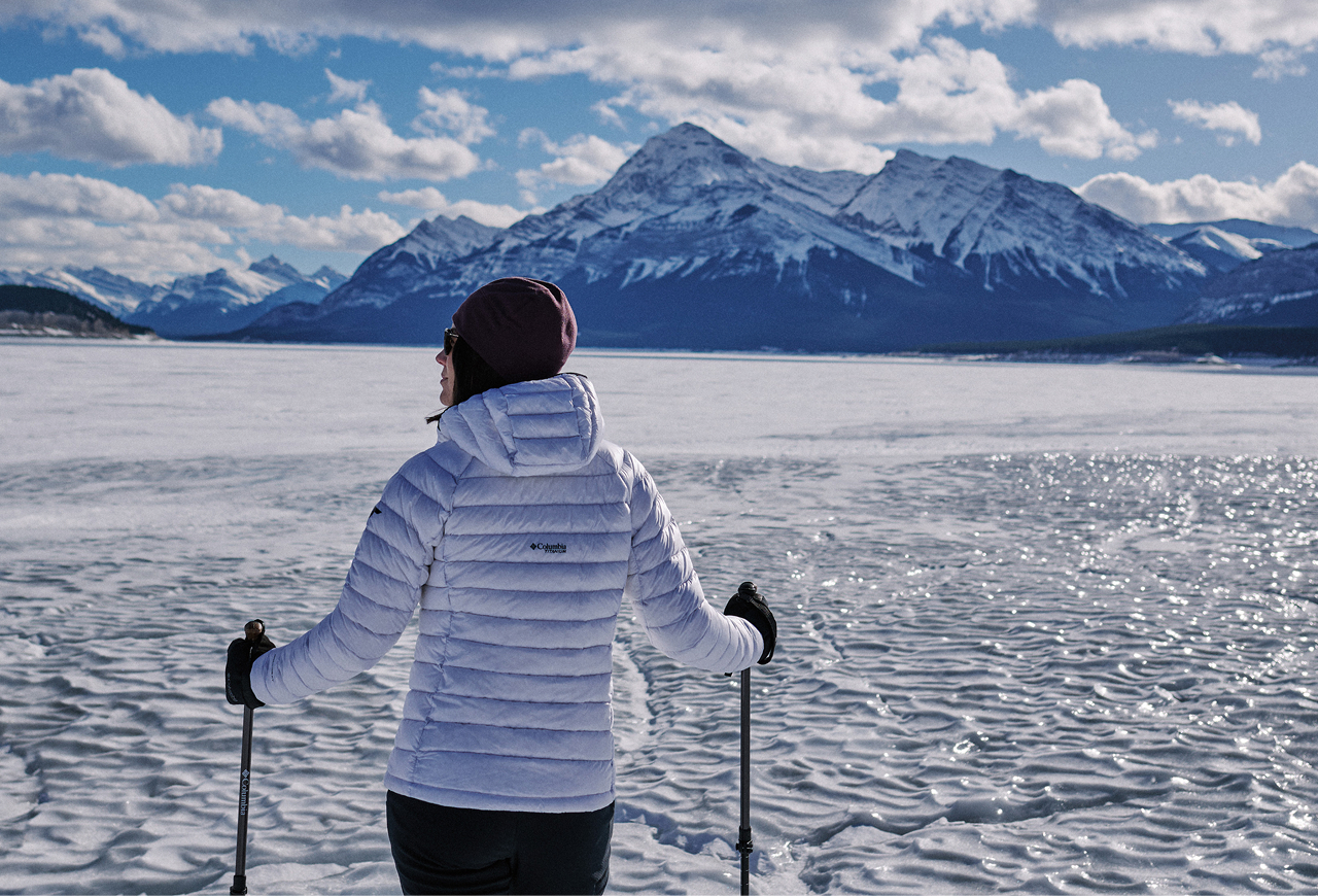 A woman wearing a white puffer against an epic icy landscape with mountains in the background.