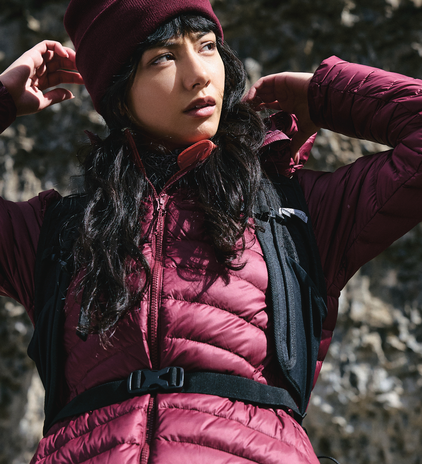 A woman wearing a maroon puffer and black backpack.
