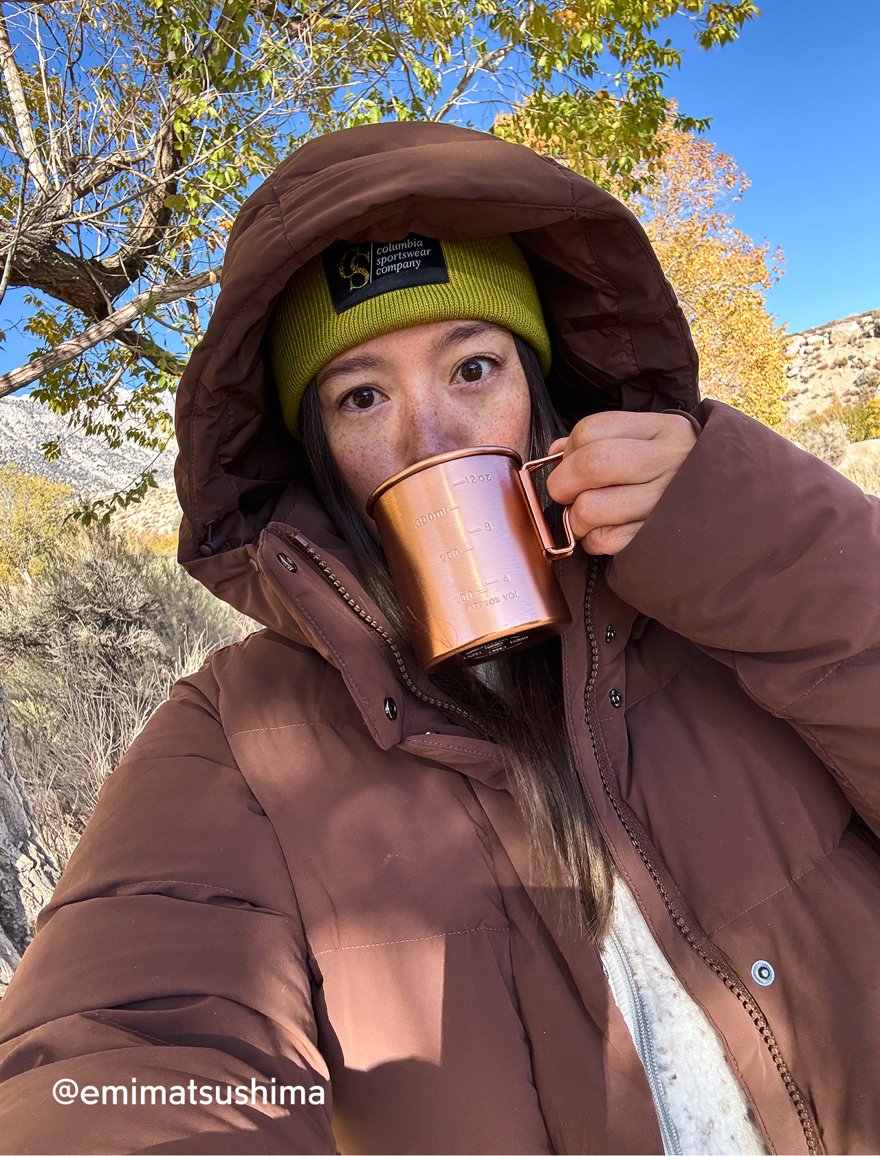A woman wearing a brown Amaze Puff and beanie drinking out of a copper mug.