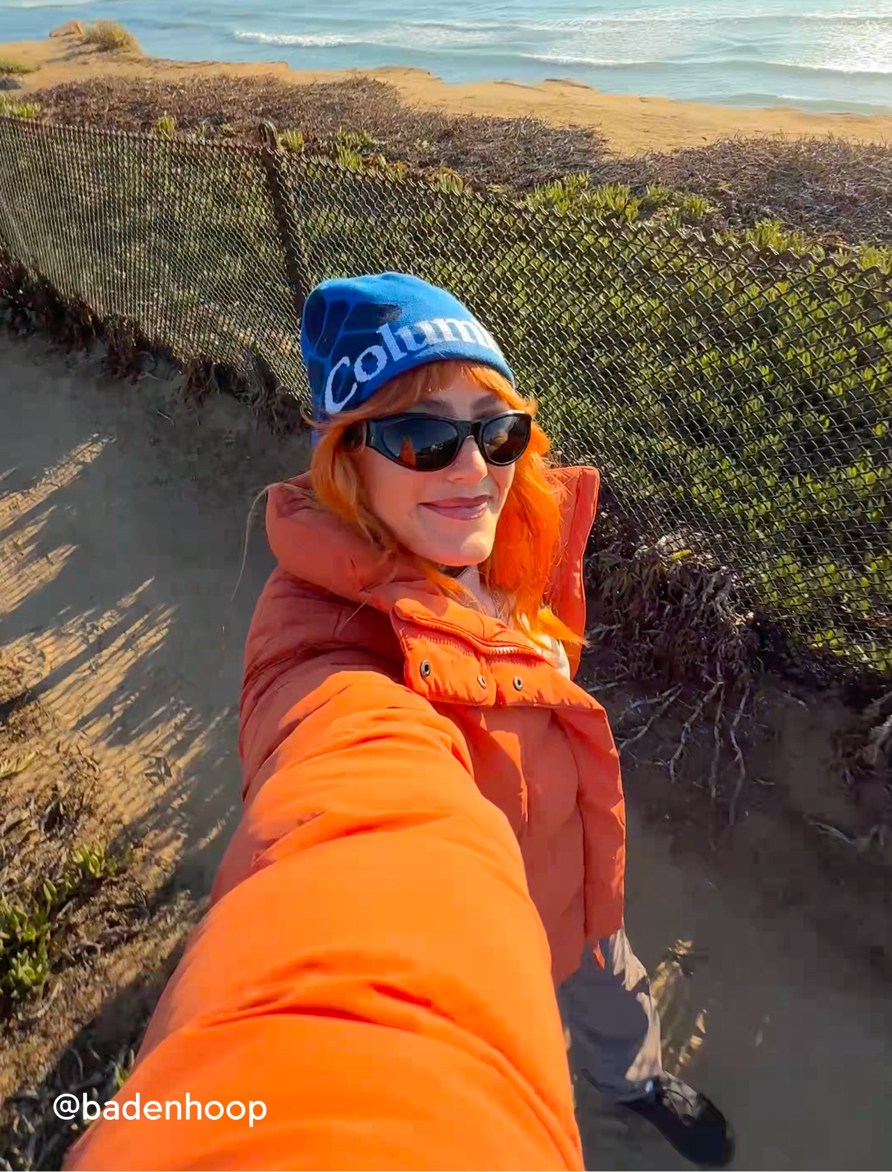 A woman on a hike wearing an orange Amaze Puff and blue beanie