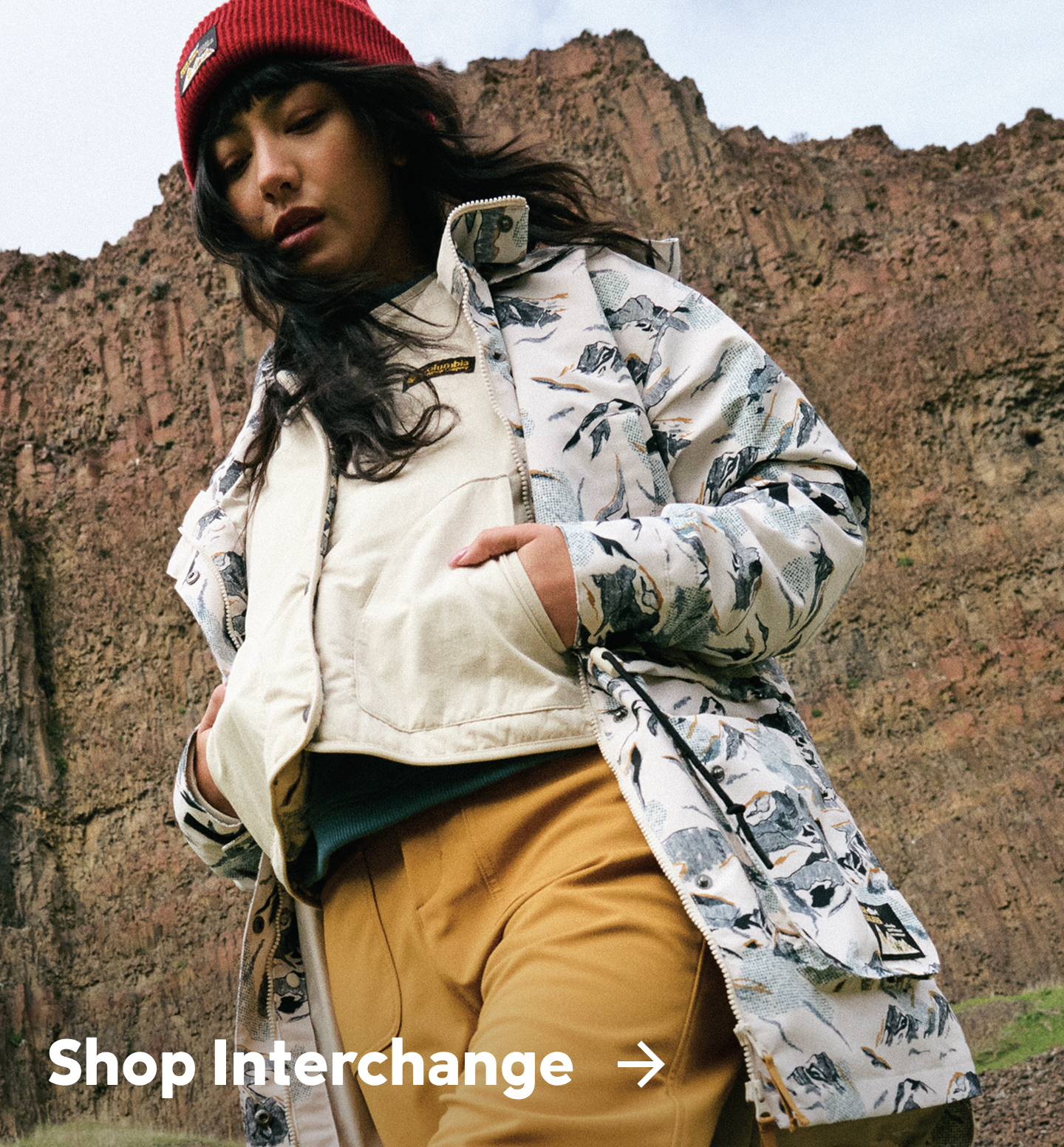 A woman wearing a white and blue pattern jacket in a rocky landscape with text: Shop Interchange
